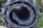 Aufgerollte Pflanzmatte aus recyceltem Granulat in Grau mit blauen Sprenkeln auf Rasen