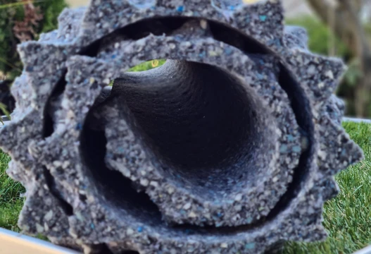 Aufgerollte Pflanzmatte aus recyceltem Granulat in Grau mit blauen Sprenkeln auf Rasen